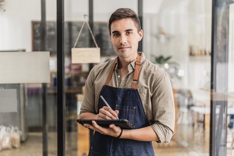 VALOR PYME_FOTOS_handsome-man-standing-holding-tablet-taking-notes-he-s-store-clerk-he-wears-apron-serves-customers-who-come-use-service-cafe-cafe-service-concept