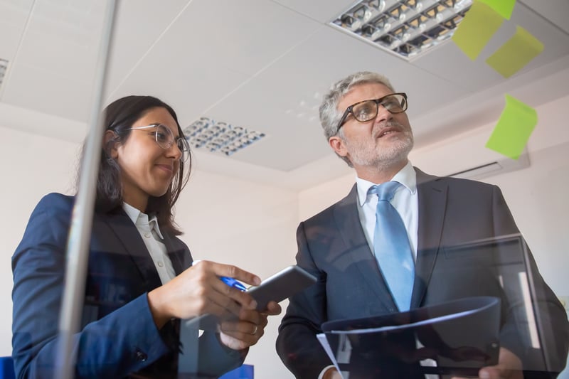 colegas-concentrados-leyendo-pegatinas-en-la-pared-de-vidrio-y-de-pie-contenido-tableta-de-explotacion-joven-empresaria-latina-hombre-barbudo-con-portapapeles-concepto-de-gestion-negocios-y-asociacion