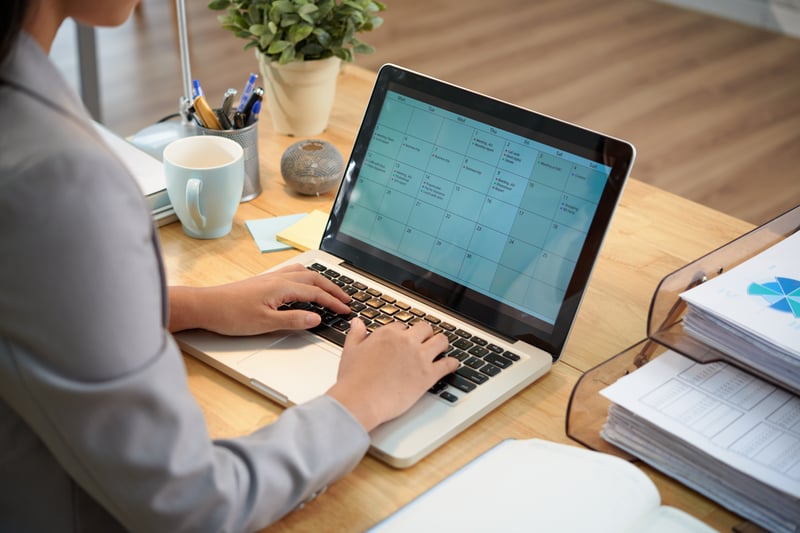 empresaria-irreconocible-sentado-en-el-escritorio-con-la-computadora-portatil-y-mirando-el-calendario
