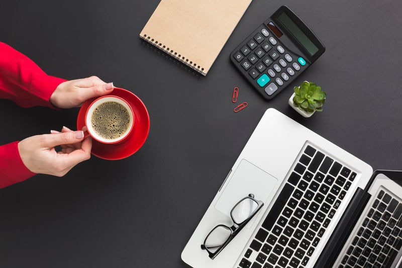 vista-superior-de-manos-sosteniendo-la-taza-de-cafe-en-la-mesa-de-trabajo